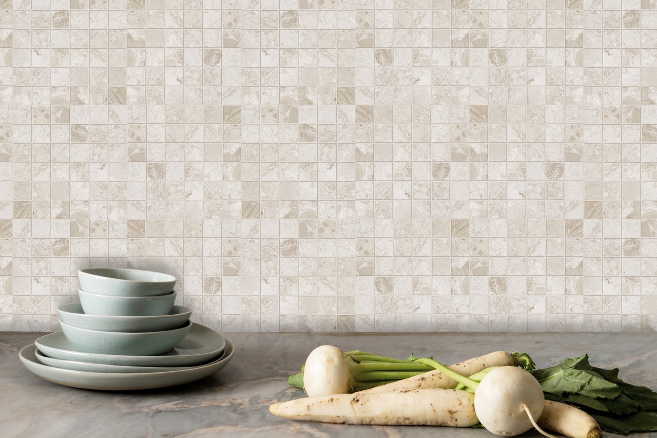 Decoratieve mozaïektegelwand met servies en groenten op een aanrecht.