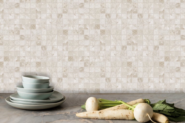 Decoratieve mozaïektegelwand met servies en groenten op een aanrecht.