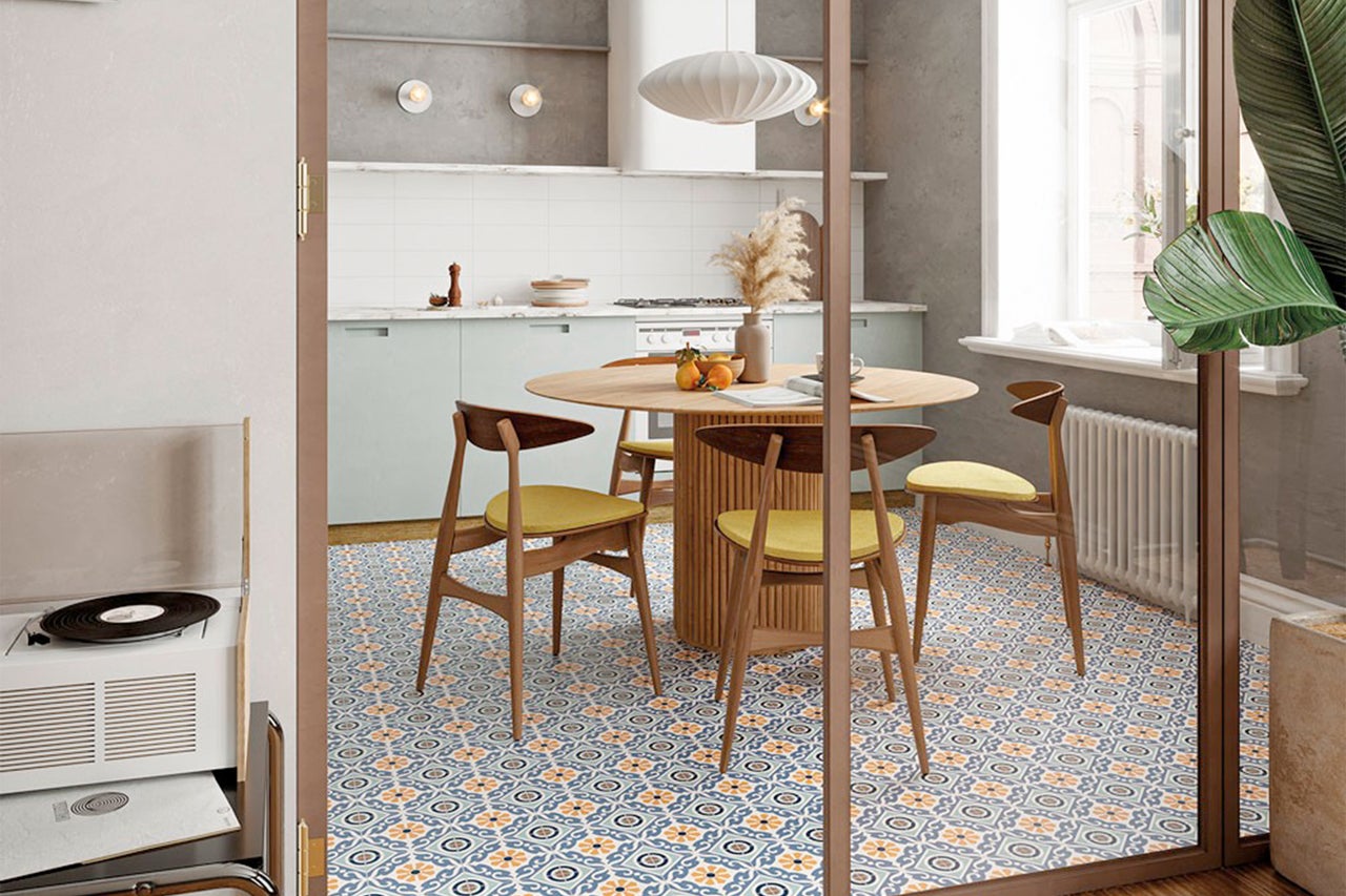 Eetkamer met ronde houten tafel, stoelen en betegelde vloer met patroon.
