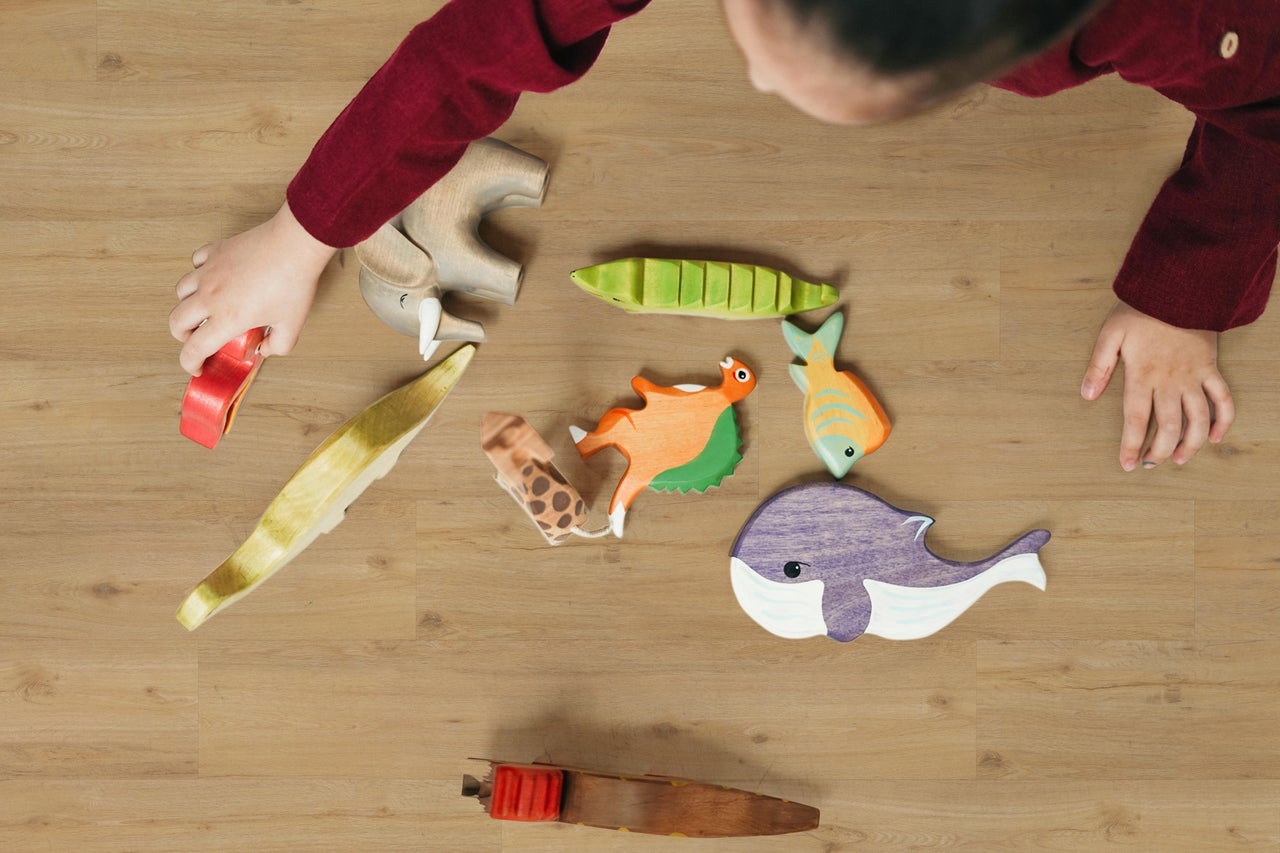 Bovenaanzicht van een kind dat speelt met houten speelgoeddieren en vissen op een houten vloer