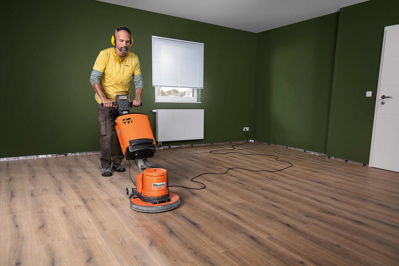 Man bedient een vloerschuurmachine in een kamer met laminaatvloer.