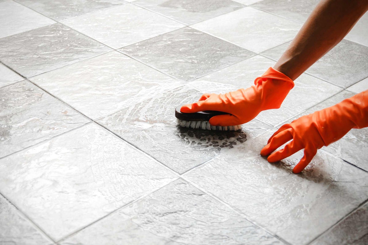 Schoonmaken van vloertegels met een borstel en handschoenen.