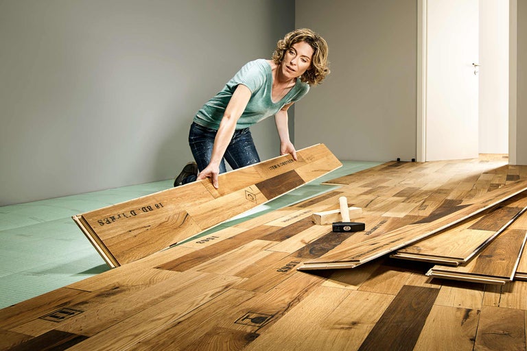 Vrouw legt houten laminaat op isolerende ondervloer binnenshuis.