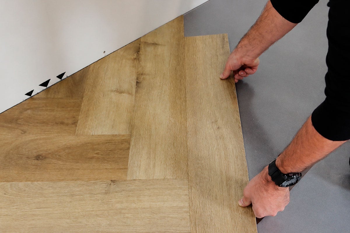 Leggen van vloerbedekking met houtlook in visgraatpatroon.