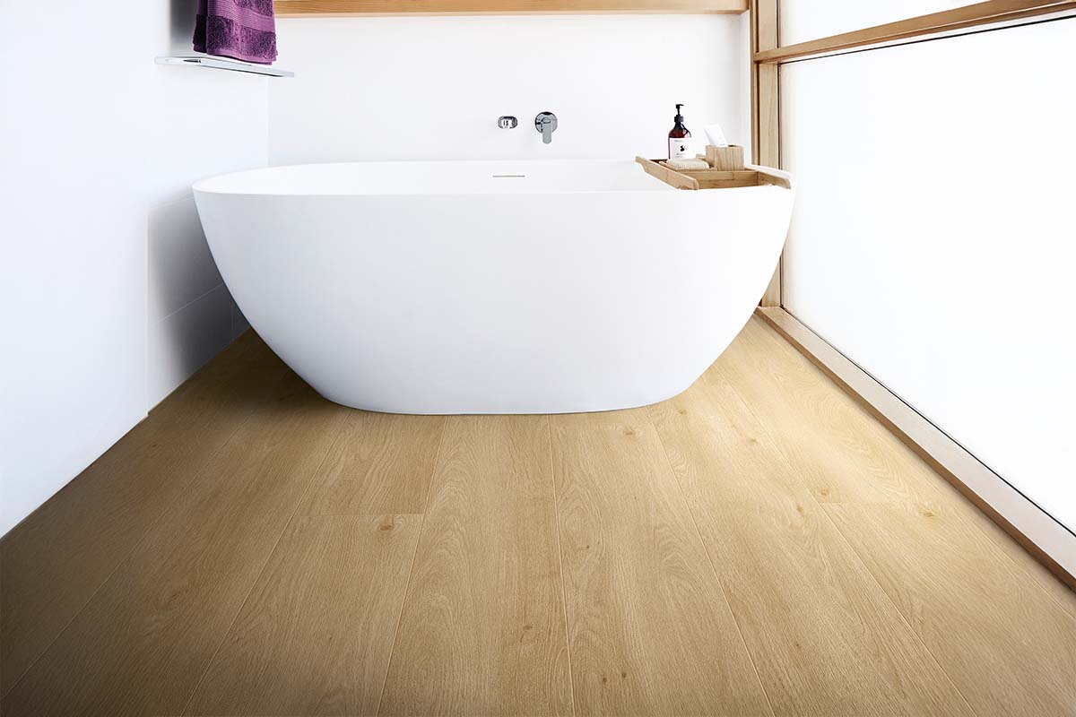 Moderne, lichte badkamer met een vrijstaand wit bad en laminaatvloer in lichte eikenlook.