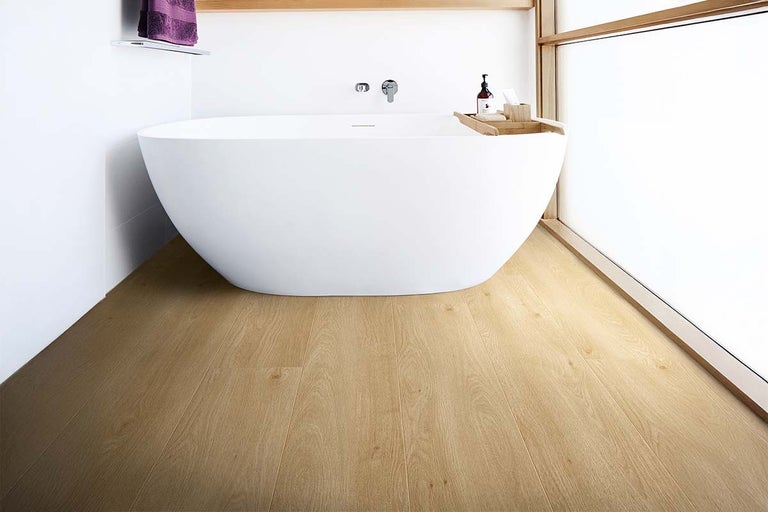Moderne, lichte badkamer met een vrijstaand wit bad en laminaatvloer in lichte eikenlook.