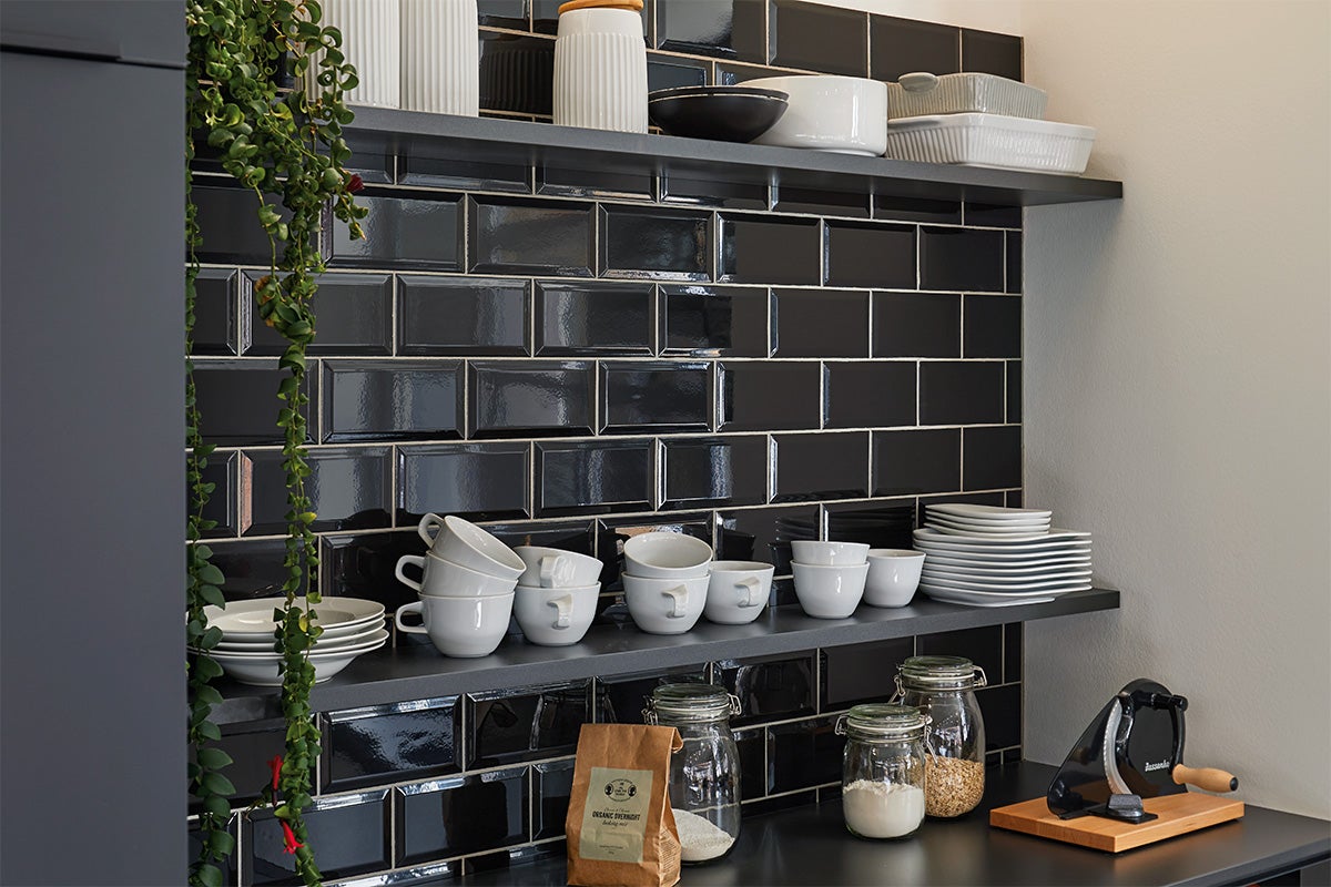 Planken met servies en levensmiddelen voor zwarte tegelwand in de keuken.