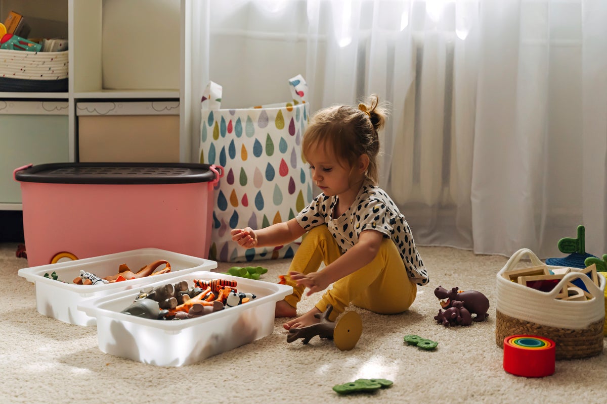Kind speelt met speelgoed in een georganiseerde kinderkamer met opbergdozen en manden.