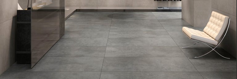 Moderne grijze vloertegels met betonlook gelegd in een ruime woonkamer met een elegante fauteuil.