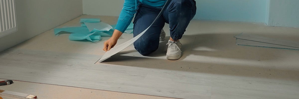 Een persoon legt een vinylvloer in een kamer door een enkel paneel op de ondergrond te plaatsen.