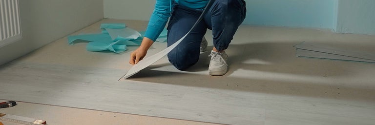 Een persoon legt een vinylvloer in een kamer door een enkel paneel op de ondergrond te plaatsen.