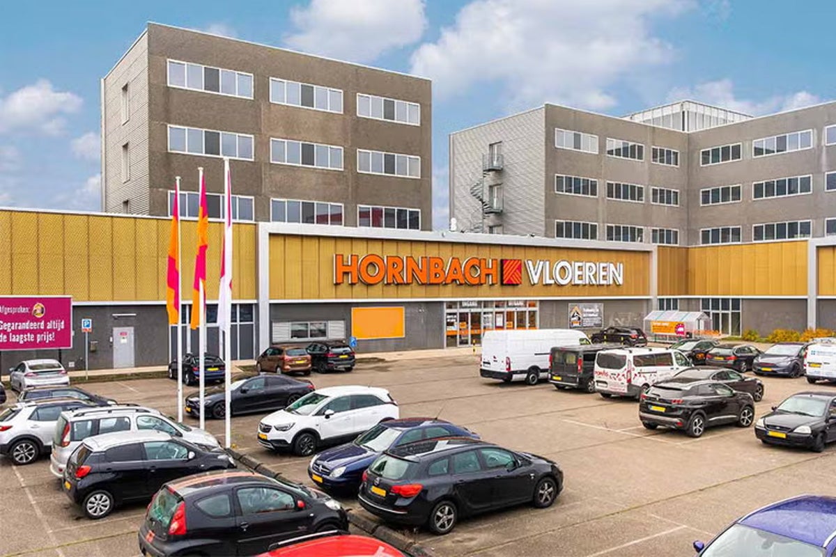 Buitenaanzicht van de Hornbach Vloeren vestiging met een parkeerplaats vol auto's voor het gebouw.