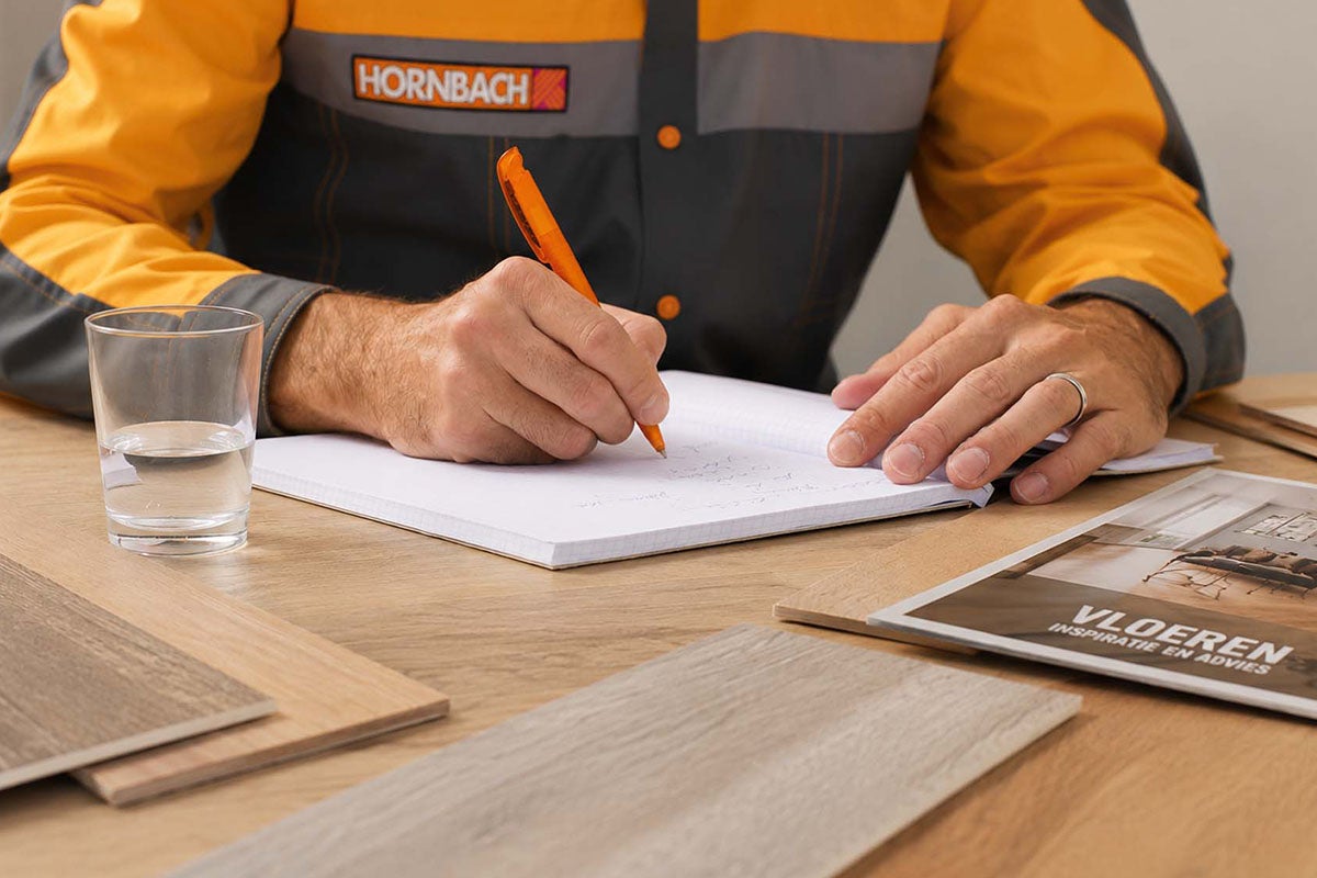 Hornbach medewerker schrijft in een notitieblok tijdens een vloeradvies met vloerstalen en een brochure op de tafel.