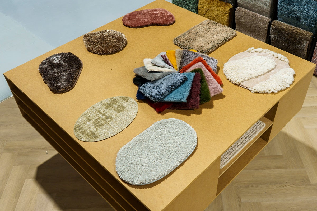 Diverse tapijtstalen in verschillende vormen en texturen gepresenteerd op een houten tafel.