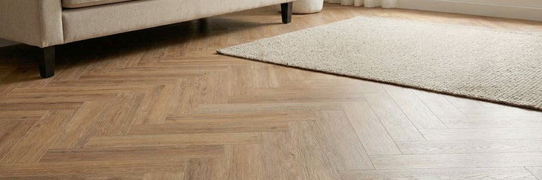 Vloer met visgraatpatroon in een lichte woonkamer met bank en vloerkleed.