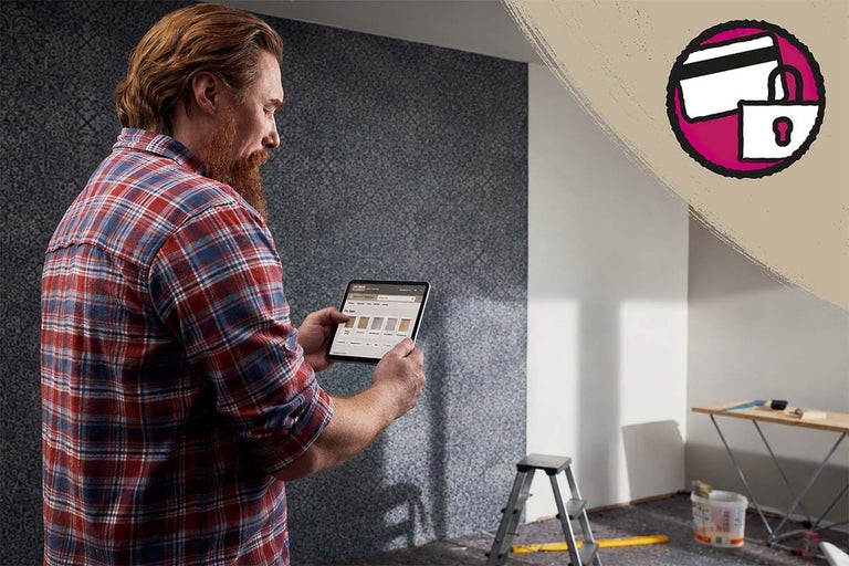 Man gebruikt tablet voor productselectie in een gerenoveerde kamer met behang met patroon en symbool voor veilig betalen.