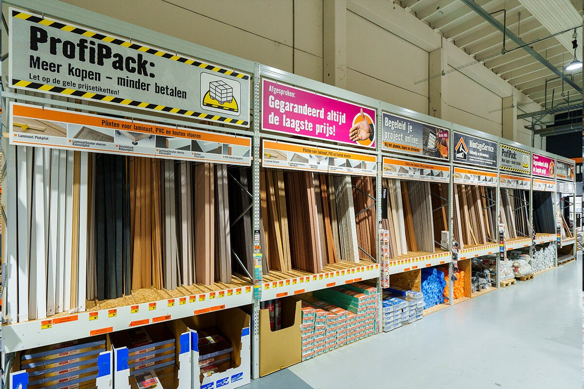 Groot winkelrek met diverse plinten voor laminaat en houten vloeren in verschillende kleuren, verticaal gesorteerd in een bouwmarkt.