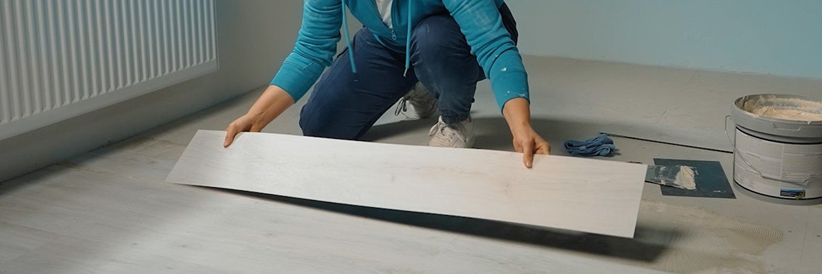 Een persoon legt een vinylvloer met houtlook door deze op de voorbereide ondergrond in een kamer te lijmen.