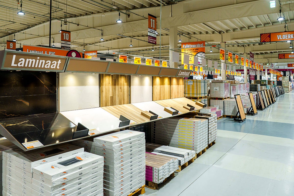 Ruime laminaatafdeling in een bouwmarkt met diverse decoren en voorraad op pallets.