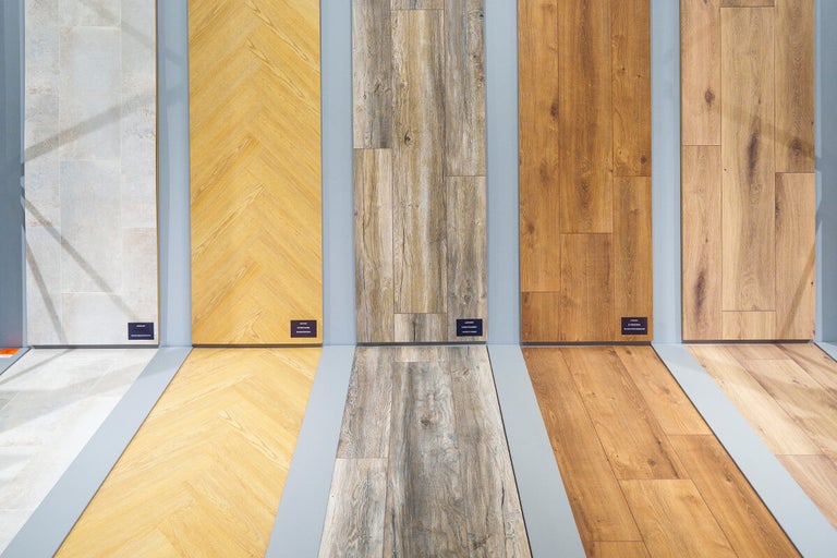 Verschillende monsters van laminaat- en vinylvloeren met houtlook, steenlook en visgraatpatroon gepresenteerd op de wand en vloer.
