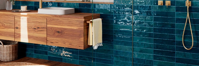 Moderne badkamer met blauwe glanzende wandtegels, houten wastafelmeubel, witte waskom en goudkleurige kranen.