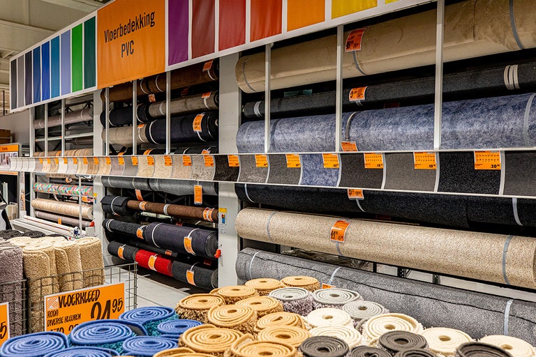 Goed georganiseerd, licht winkelschap met diverse rollen pvc-vloerbedekking en tapijt in verschillende designs en materialen.