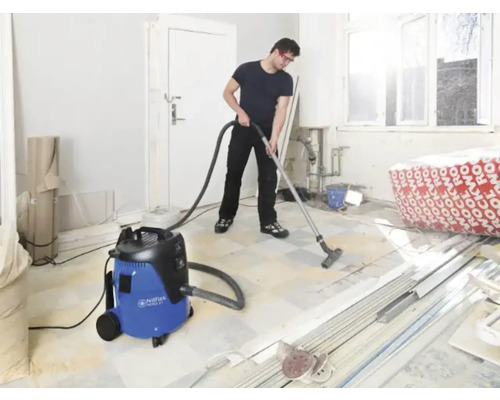 Man zuigt een kamer met een nat- en droogzuiger. Op de achtergrond zijn bouwmaterialen te zien.