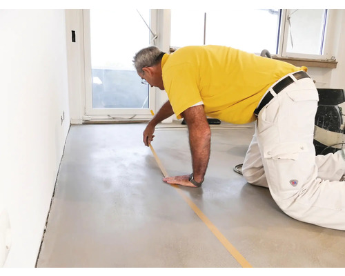Man plakt afplakband op een vloer voor renovatiewerkzaamheden.