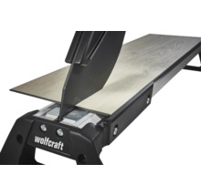 Wolfcraft laminaatsnijder snijdt een laminaatplank met houtstructuur. Detailweergave van het snijmechanisme.