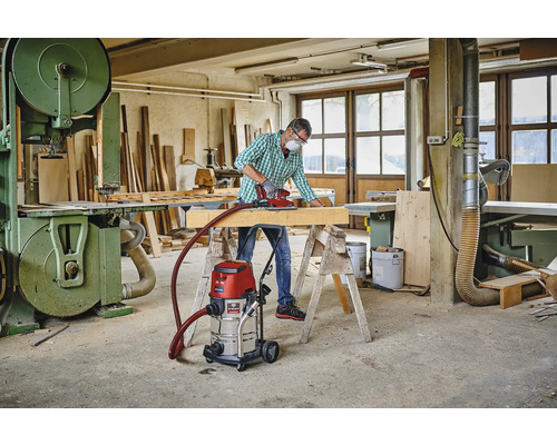 Werkplaats met vakman, schuurmachine, houten balk, werkbank, industriële stofzuiger en lintzaag