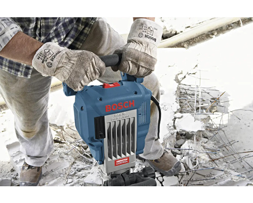 Een bouwvakker met handschoenen bedient een Bosch GSH 16 Professional breekhamer op een bouwplaats.