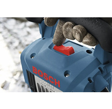 Hand met handschoen bedient de rode schakelaar van een blauwe Bosch breekhamer.