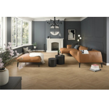 Ruime moderne woonkamer met vloer met houtlook in visgraatmotief, wanden met sierlijsten, een grote leren bank en een schouw.