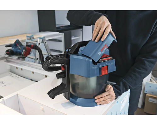 Een persoon plaatst een 18 Volt accu in een Bosch Professional accu stofzuiger GAS 18 Volt-1 in een werkplaats.