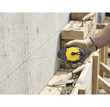 Vakman markeert met een slaglijnmolen een rechte lijn op een betonnen muur op een bouwplaats met metselwerk.