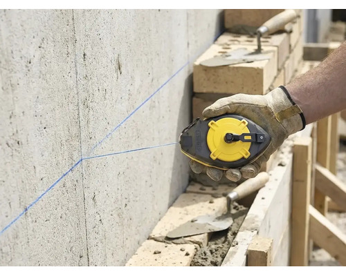 Vakman markeert met een slaglijnmolen een rechte lijn op een betonnen muur op een bouwplaats met metselwerk.