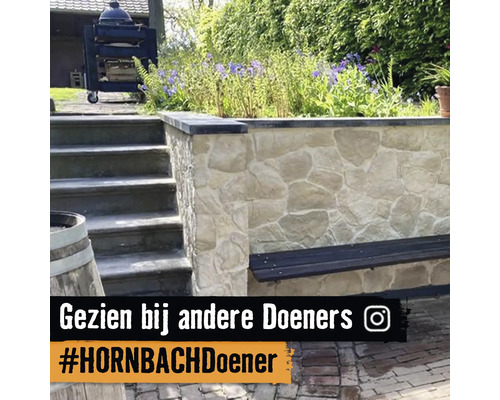 Tuininrichting met een natuurstenen muur, een geïntegreerde houten bank en stenen trappen naast een bloemborder.