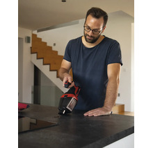 Een man gebruikt een Einhell kruimeldief om koffiebonen op te zuigen van een aanrecht in een lichte, moderne woning.