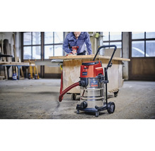 Einhell nat droogzuiger met roestvrijstalen reservoir in gebruik in een werkplaats met vakman op de achtergrond.