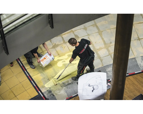 Vakman brengt primer aan met een verfroller op een tegelvloer binnenshuis.