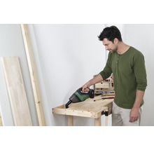 Een man stofzuigt een houten werkbank met een draadloze handstofzuiger.
