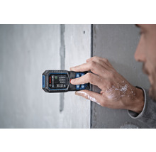 Een persoon gebruikt een Bosch afstandsmeter op een muur voor metingen.