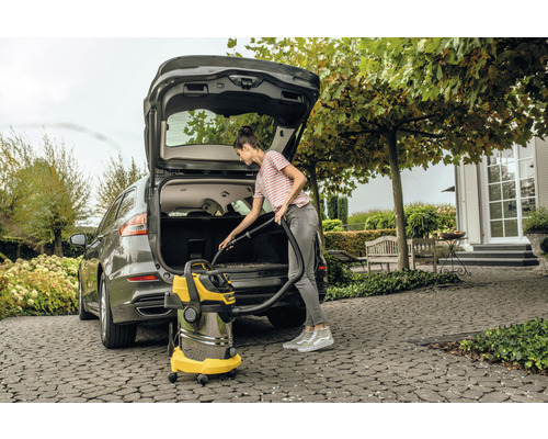 Een vrouw maakt met een alleszuiger de kofferbak van een auto schoon.