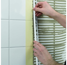 Een man bevestigt een tegelprofiel aan een wand met tegels.