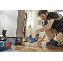 Ambachtsman werkt met een Bosch voegensnijder op een houten vloer, op de achtergrond een plank en een gereedschapskist.