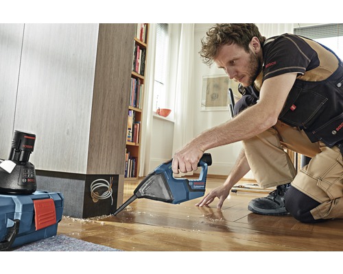 Ambachtsman werkt met een Bosch voegensnijder op een houten vloer, op de achtergrond een plank en een gereedschapskist.