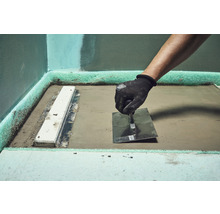 Vakman bewerkt dekvloer met een troffel in een badkamer