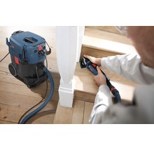 Een persoon gebruikt een multifunctionele schuurmachine om een houten trap te schuren, met een stofzuiger voor een schone werkomgeving.