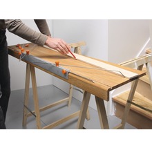 Persoon tekent een houten plank met een potlood op een werkbank.