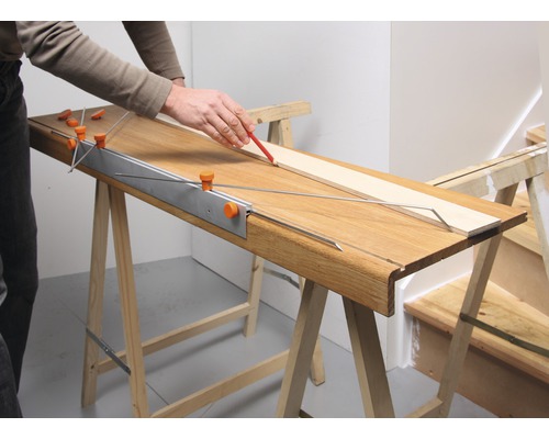 Persoon tekent een houten plank met een potlood op een werkbank.